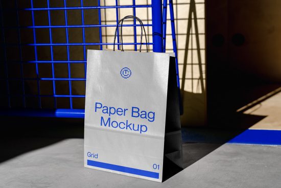 Realistic paper bag mockup on a concrete floor against a blue grid background, ideal for branding and packaging design presentations.